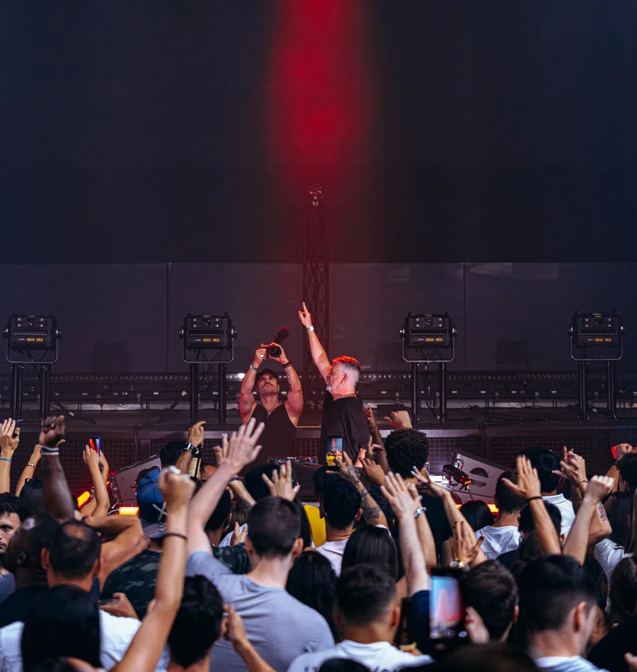 DJ INO on stage with the crowd’s hands up under a red light beam